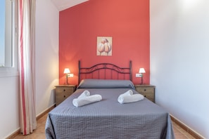 A bedroom with a bed, two bedside tables, a nightstand, a window with curtains, and a wall painting. - Apartment 'Fran' with Shared Pool and Terrace (Conil de la Frontera)