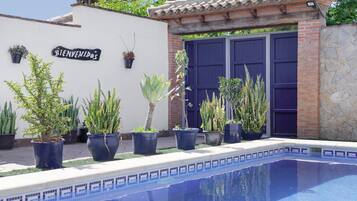 A pool area with a 'BIENVENIDOS' sign, potted plants, and a blue door.