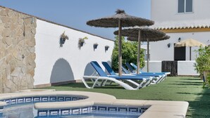 A swimming pool with lounge chairs, a stone wall, and a white building with a tiled roof. - Apartment 'Fran' with Shared Pool and Terrace (Conil de la Frontera)