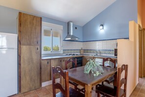 A kitchen with wooden cabinets, a dining table with chairs, a built-in stove, and a window with blinds. - Apartment 'Fran' with Shared Pool and Terrace (Conil de la Frontera)