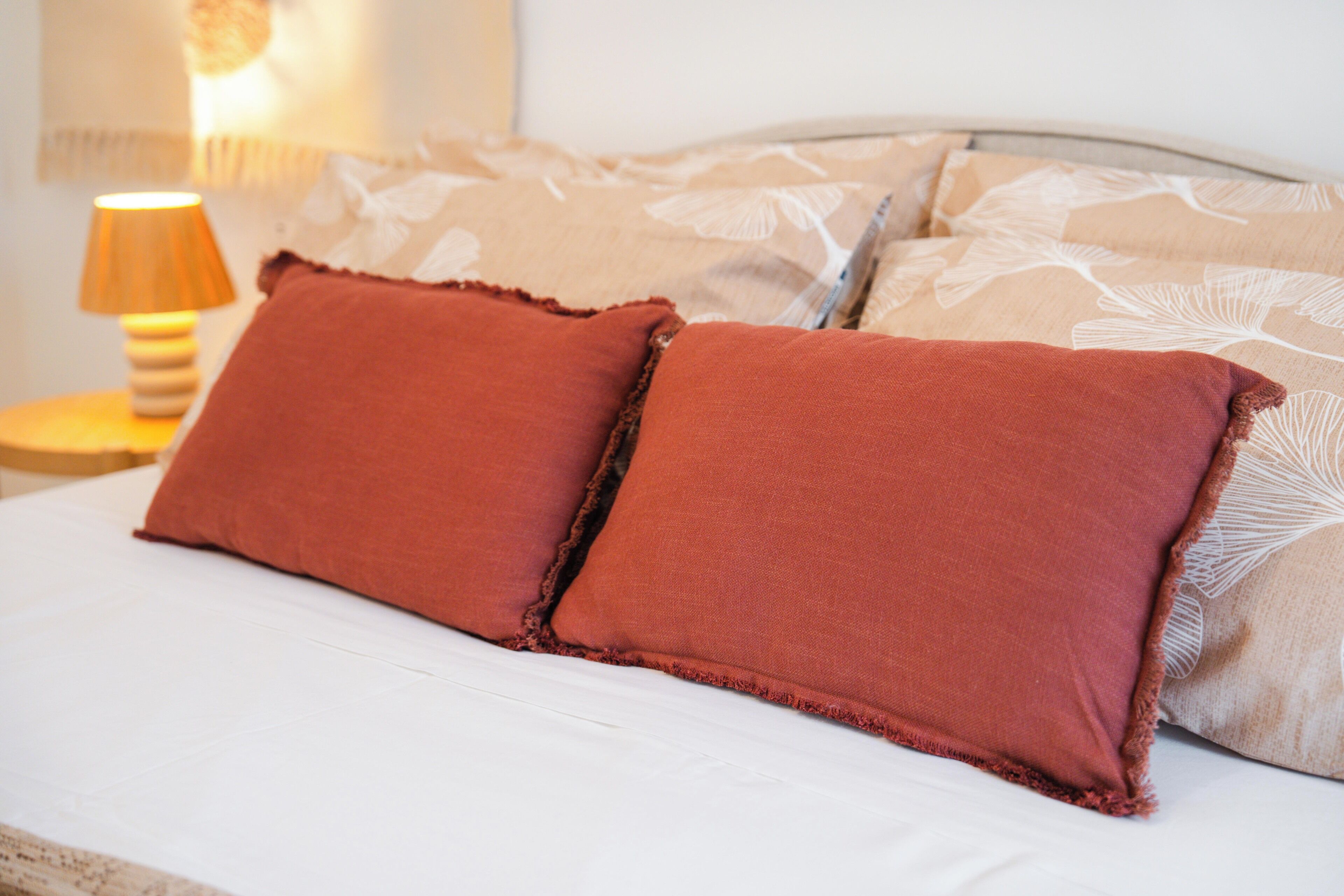 A bed with two red pillows and a patterned pillow on a white mattress.