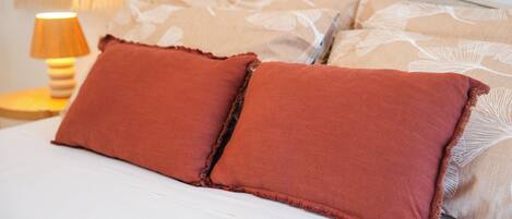 A bed with two red pillows and a patterned pillow on a white mattress.