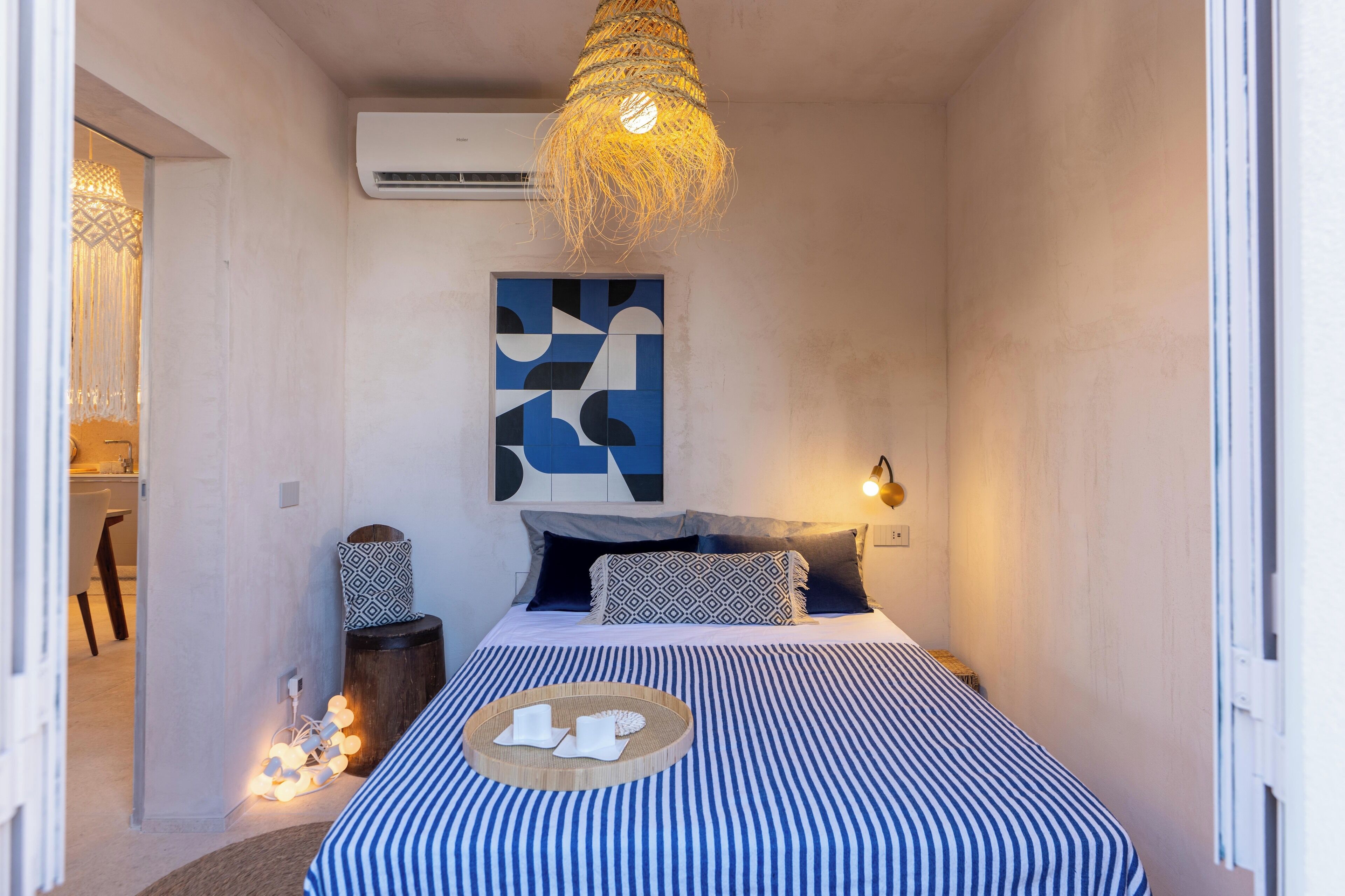 A bedroom with a bed, a hanging light fixture, an air conditioner, and a wall-mounted artwork.