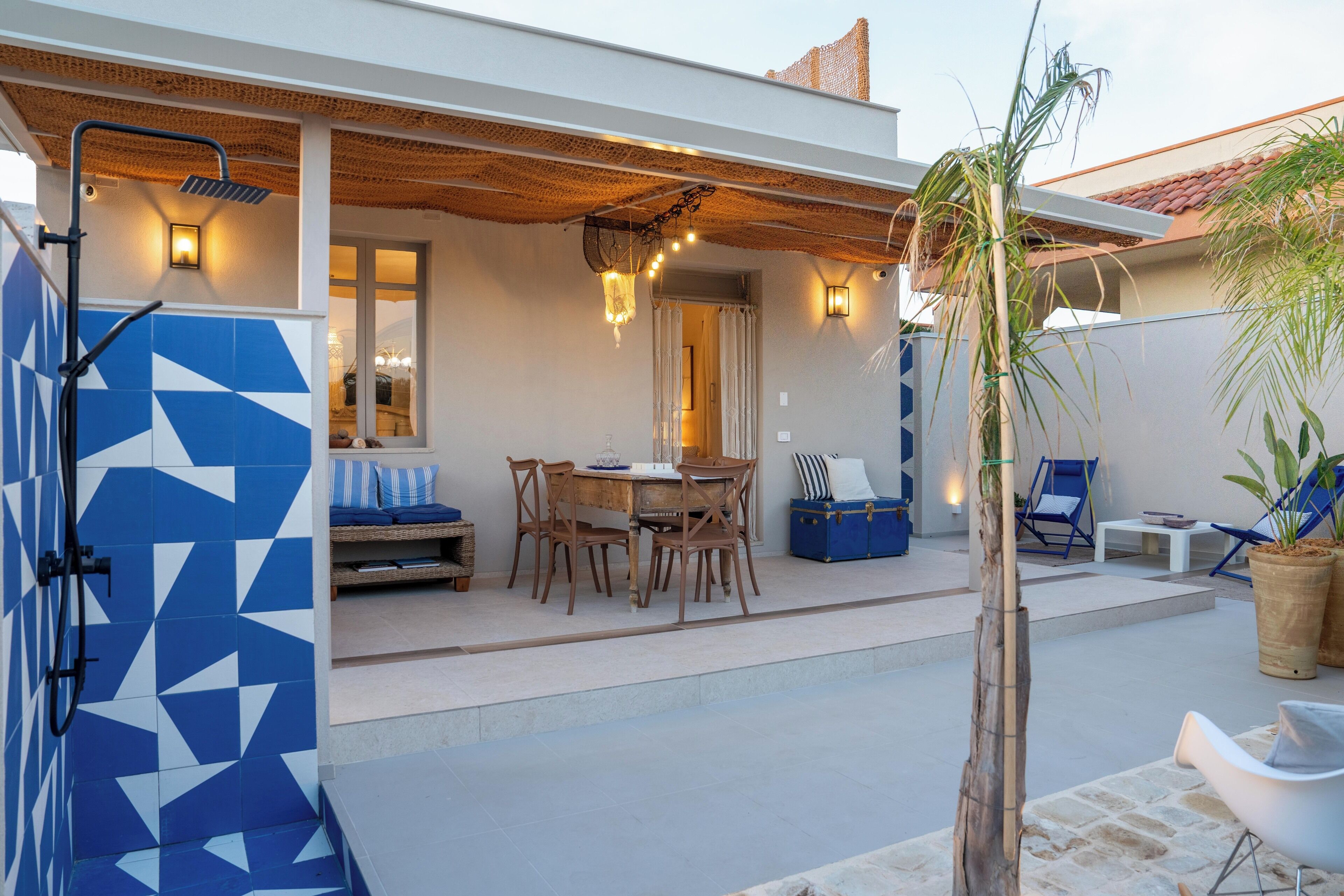 Un espacio al aire libre techado con una mesa, sillas, un muro de azulejos azules y blancos, y un banco de madera.