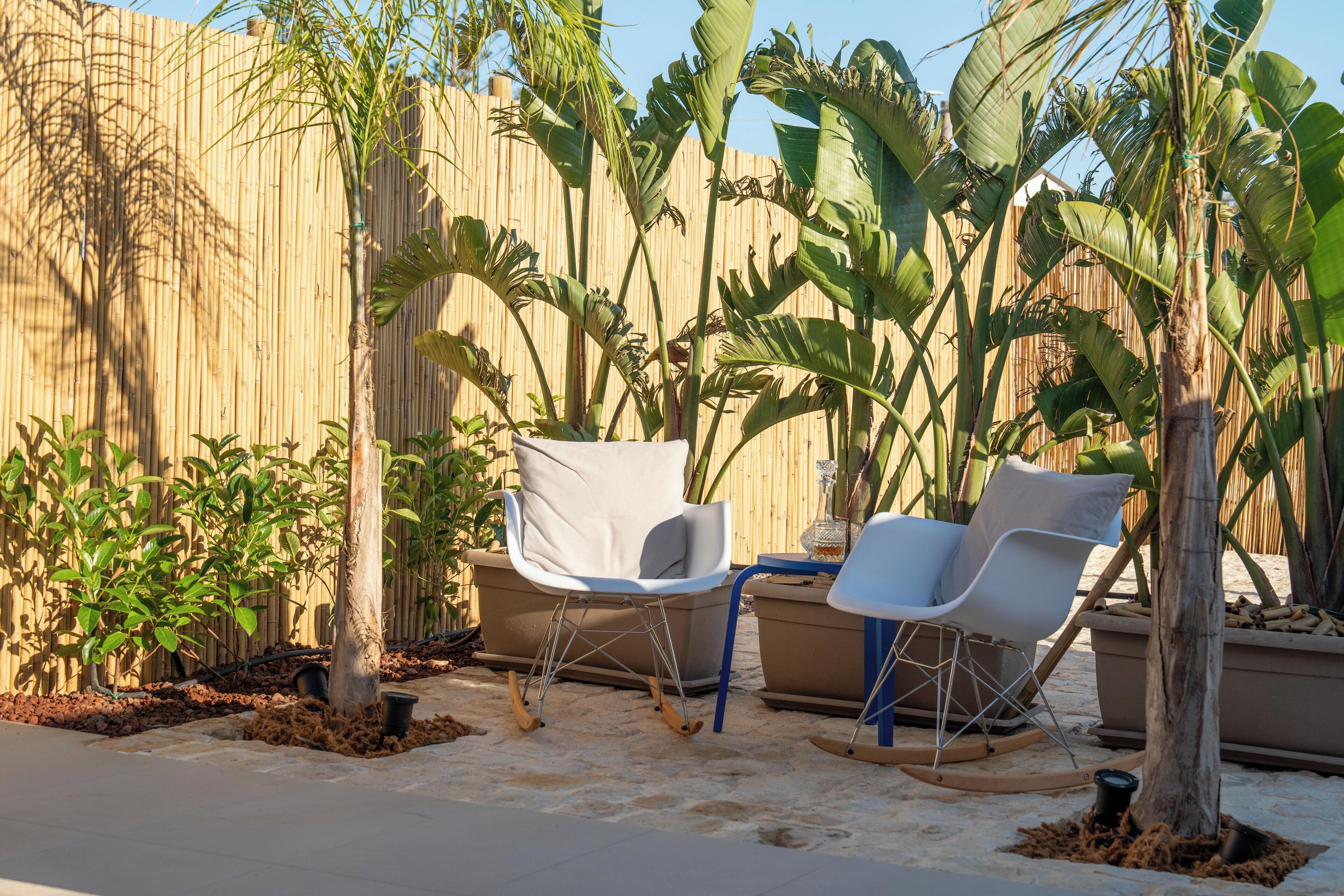A patio area with two white chairs, a small table, and a bamboo fence.