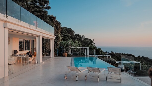 Ein moderner Poolbereich im Freien mit Glasgeländern, Liegestühlen und Blick auf das Meer.