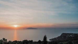 Eine Küstenlandschaft mit Sonnenuntergang über dem Wasser, entfernten Inseln und einer felsigen Klippe mit Vegetation.