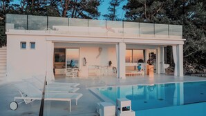 Ein modernes Haus mit Schwimmbad, das eine überdachte Glasveranda, Sitzgelegenheiten im Freien und einen Skulpturengarten bietet.
