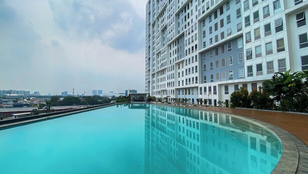A large, rectangular swimming pool with a curved edge, surrounded by a low brick wall. - Comfy And Tidy Studio At Patraland Urbano Apartment (Bekasi)