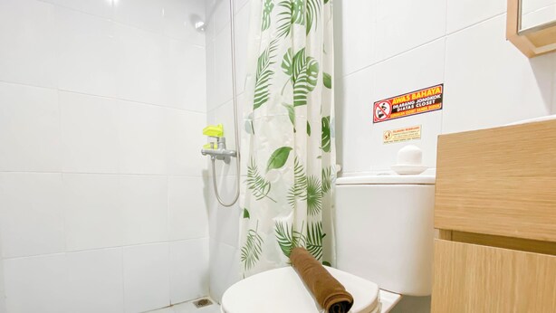 Un baño con inodoro, cortina de ducha estampada con hojas y un letrero en la pared.