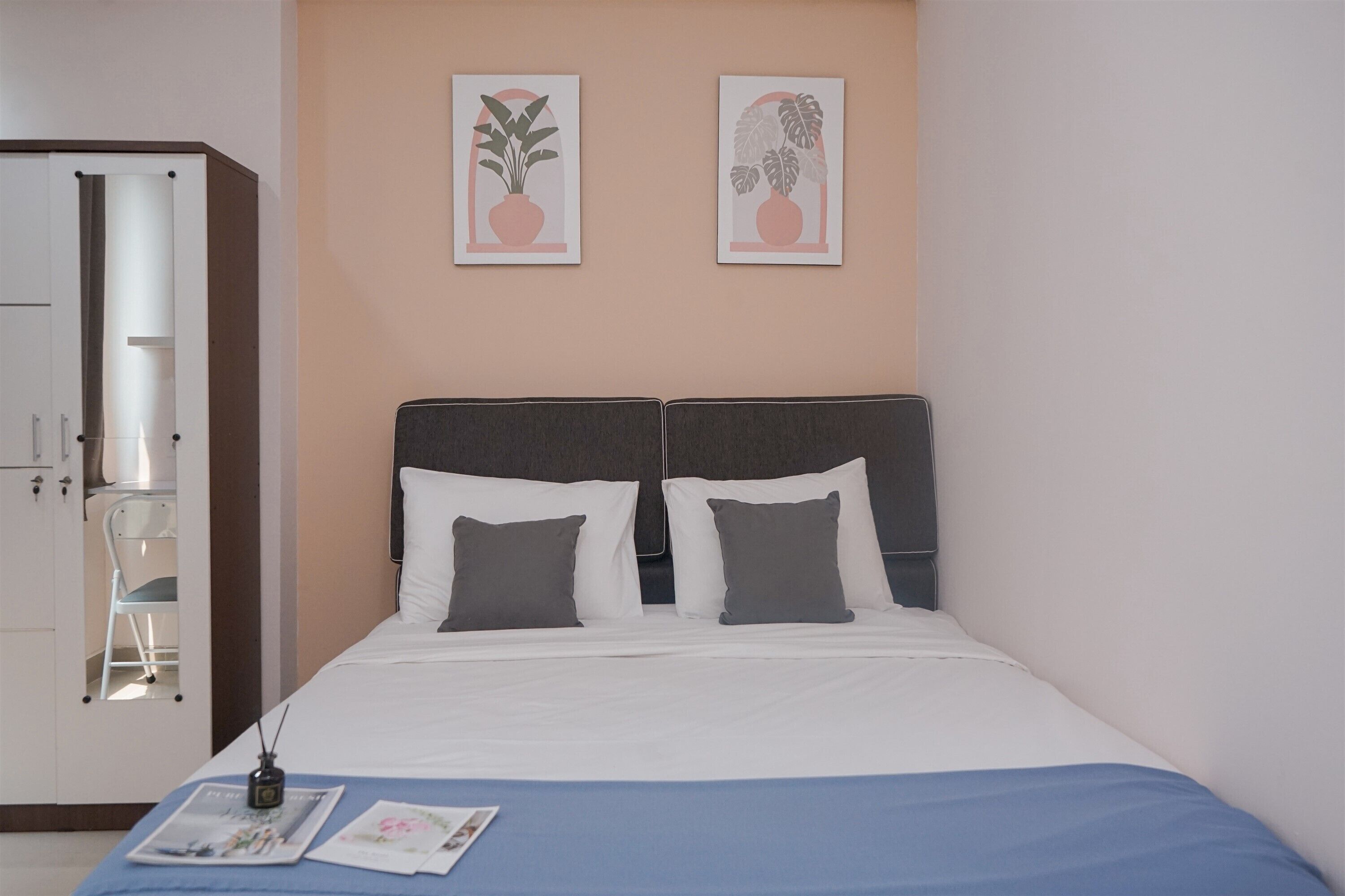 Une chambre à coucher avec un lit, deux oreillers, une table de chevet, un magazine et deux tableaux encadrés accrochés au mur.