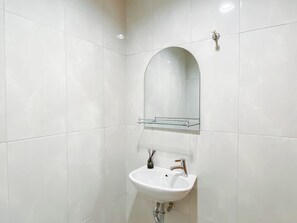 Un baño con paredes de azulejos blancos, un lavamanos blanco y un espejo sobre él.