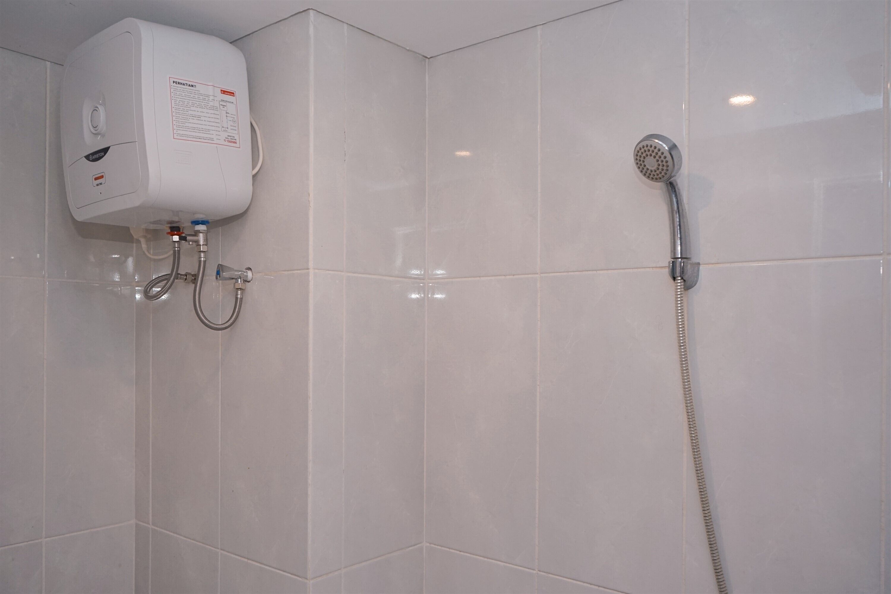 A bathroom with a white tiled wall, a built-in water heater, and a shower with a handheld showerhead.