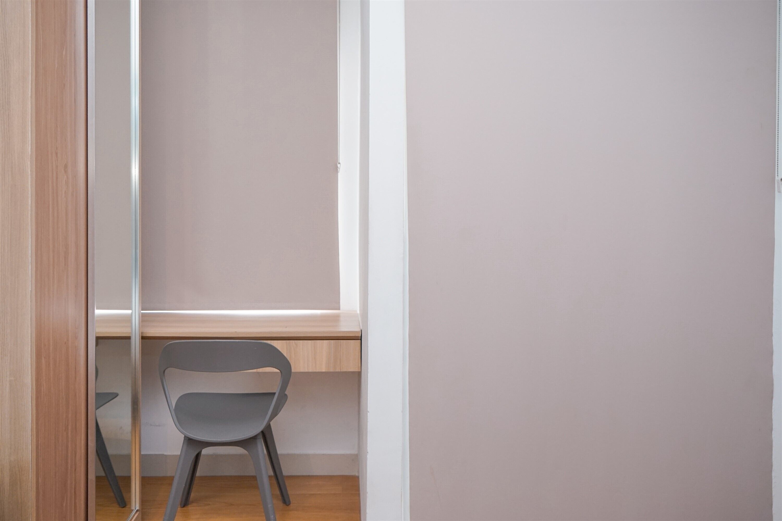 A room with a wooden floor, a grey chair, a white wall, and a window.
