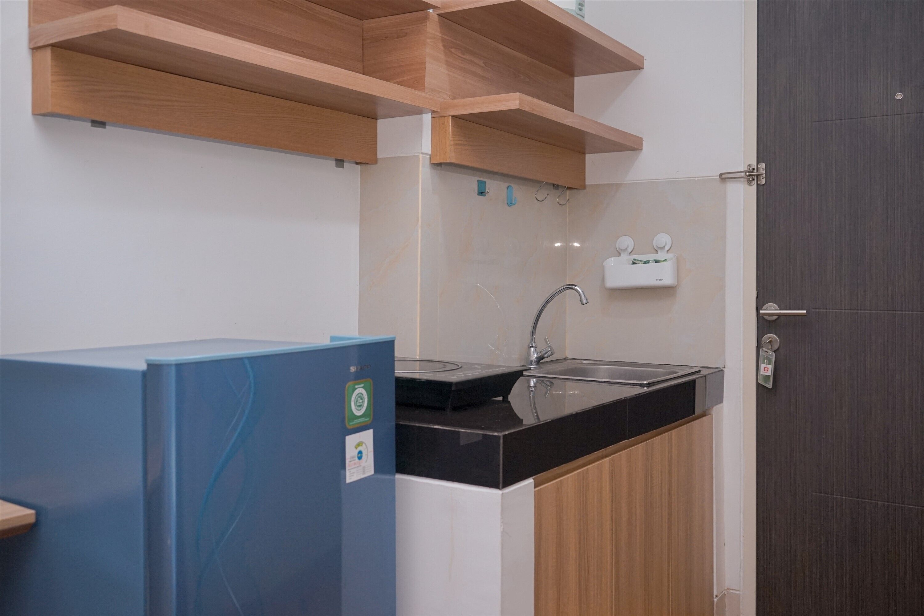 Cozinha compacta com pia, armários de madeira e geladeira azul.