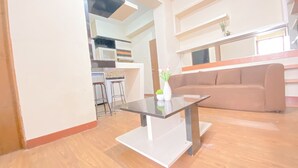 Una sala de estar moderna con una mesa de centro de vidrio, un sofá color beige y una cocina al fondo.