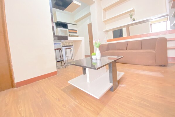 Una sala de estar moderna con una mesa de centro de vidrio, un sofá color beige y una cocina al fondo.