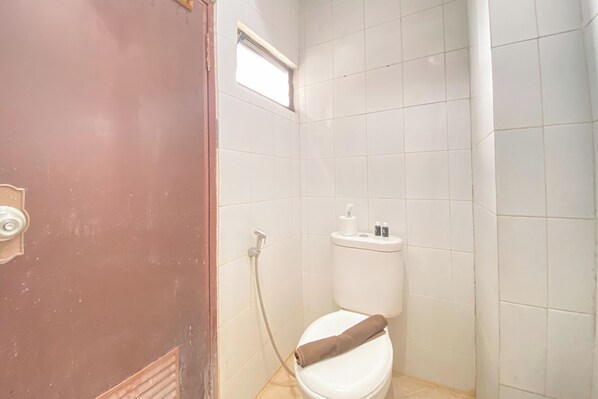 Un baño pequeño y funcional con azulejos blancos, inodoro, ducha y ventana.
