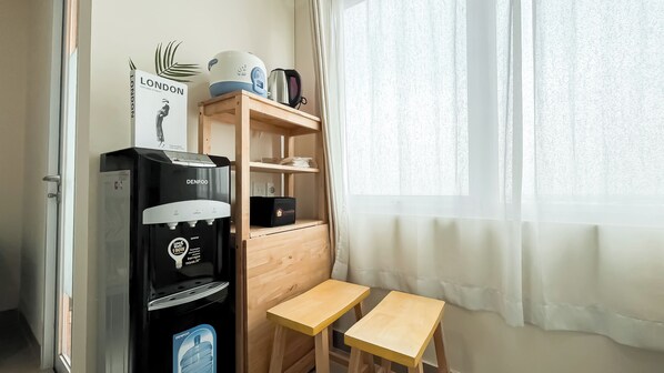 Une petite pièce équipée d’un distributeur d’eau, d’une petite table en bois et d’une étagère contenant des articles de voyage.