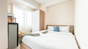 Habitación de hotel con cama, escritorio, armario y refrigerador.