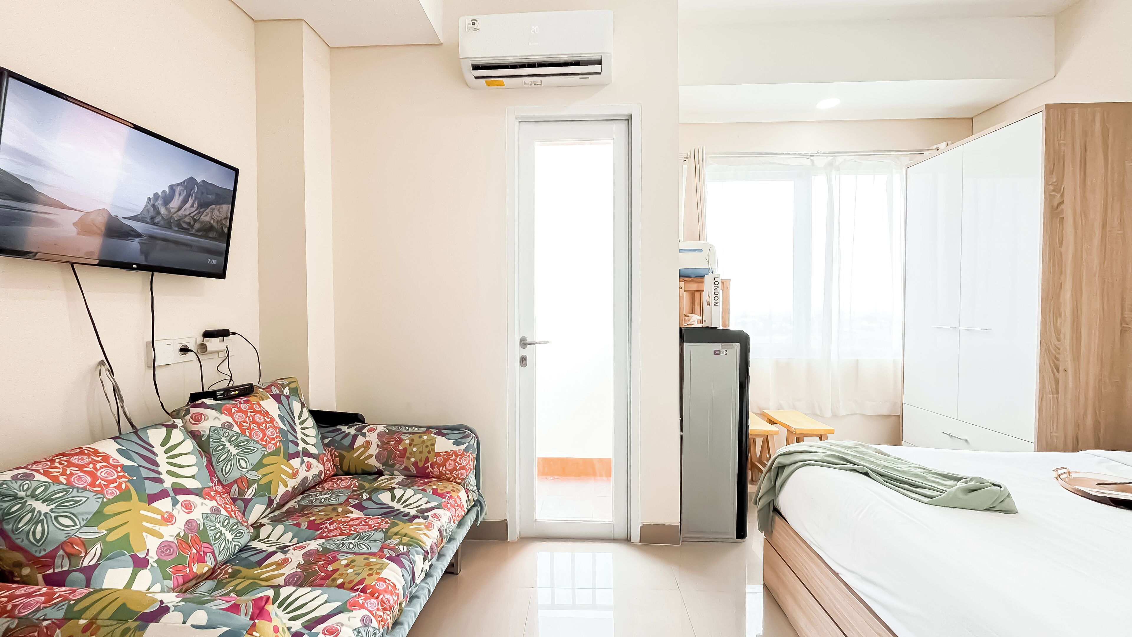 A modern hotel room with a sofa, bed, wardrobe, and a television mounted on the wall.