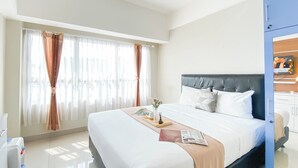 A hotel room with a large bed, a bedside table, a mirror, and a window with curtains. - Restful Studio Apartment At Springlake Summarecon Bekasi (Bekasi)
