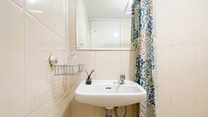 A bathroom with a white sink, a mirror, a glass soap dispenser, and a patterned shower curtain. - Restful Studio Apartment At Springlake Summarecon Bekasi (Bekasi)