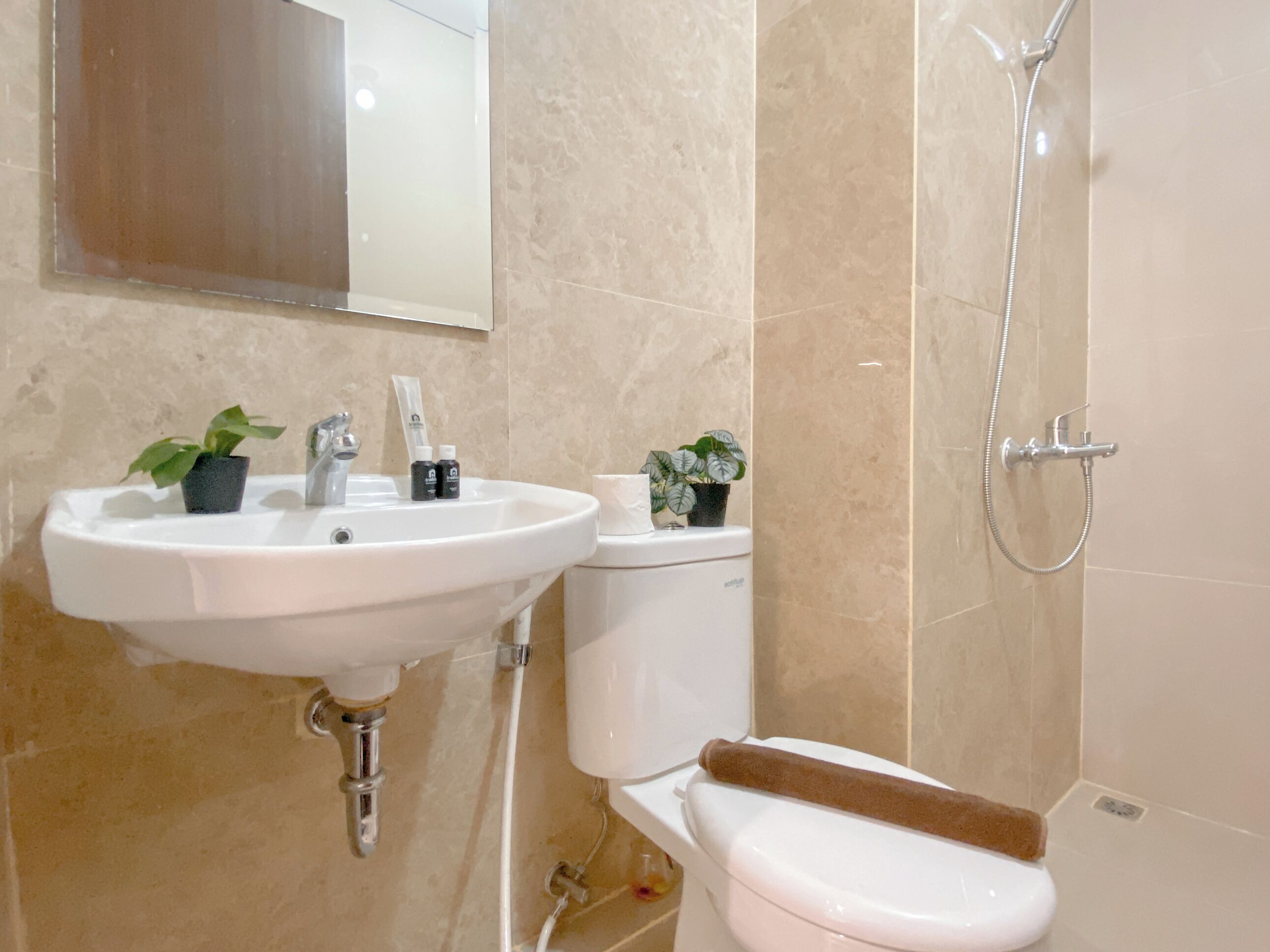 A bathroom with a white sink, toilet, and shower. There are two potted plants on the sink counter.