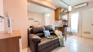 A modern living room with a brown leather sofa, a small table, and a kitchen area with a countertop and cabinets. - Simply 2Br Apartment At Green Bay Pluit (Jakarta)