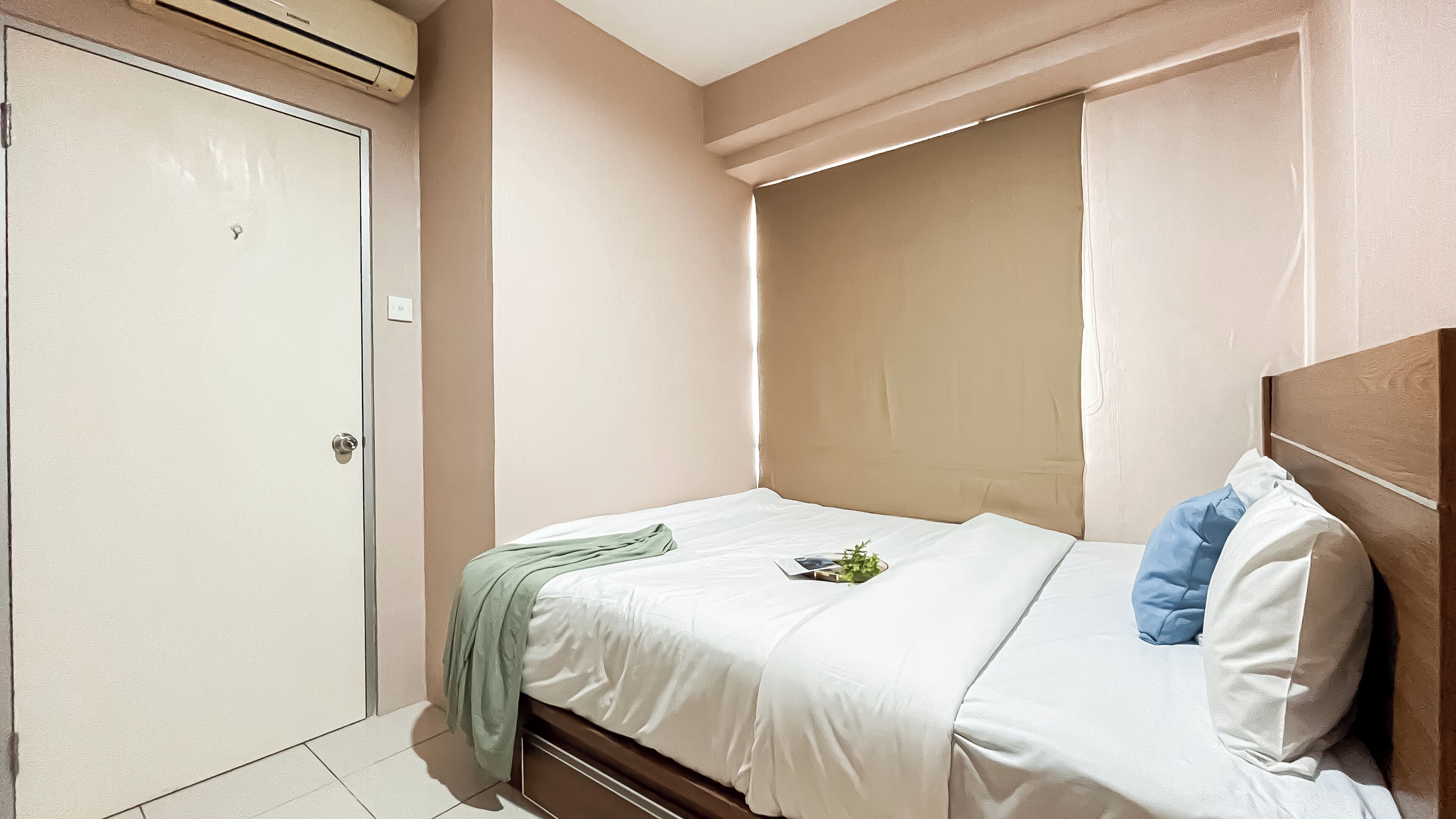 A small, neatly arranged bedroom with a single bed, a closed door, and an air conditioning unit above it.