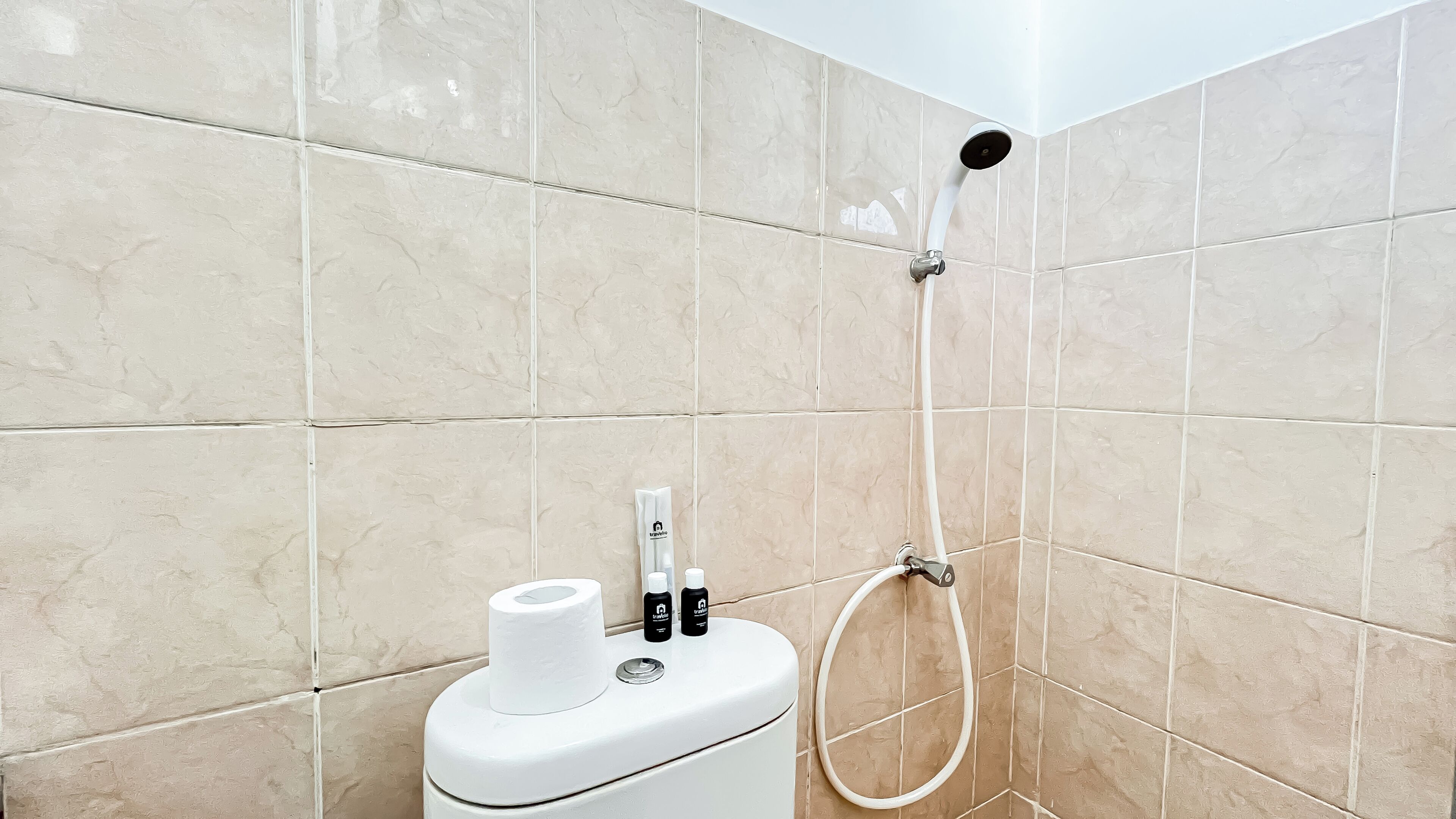 A bathroom with beige tiled walls, a white toilet, and a handheld showerhead.