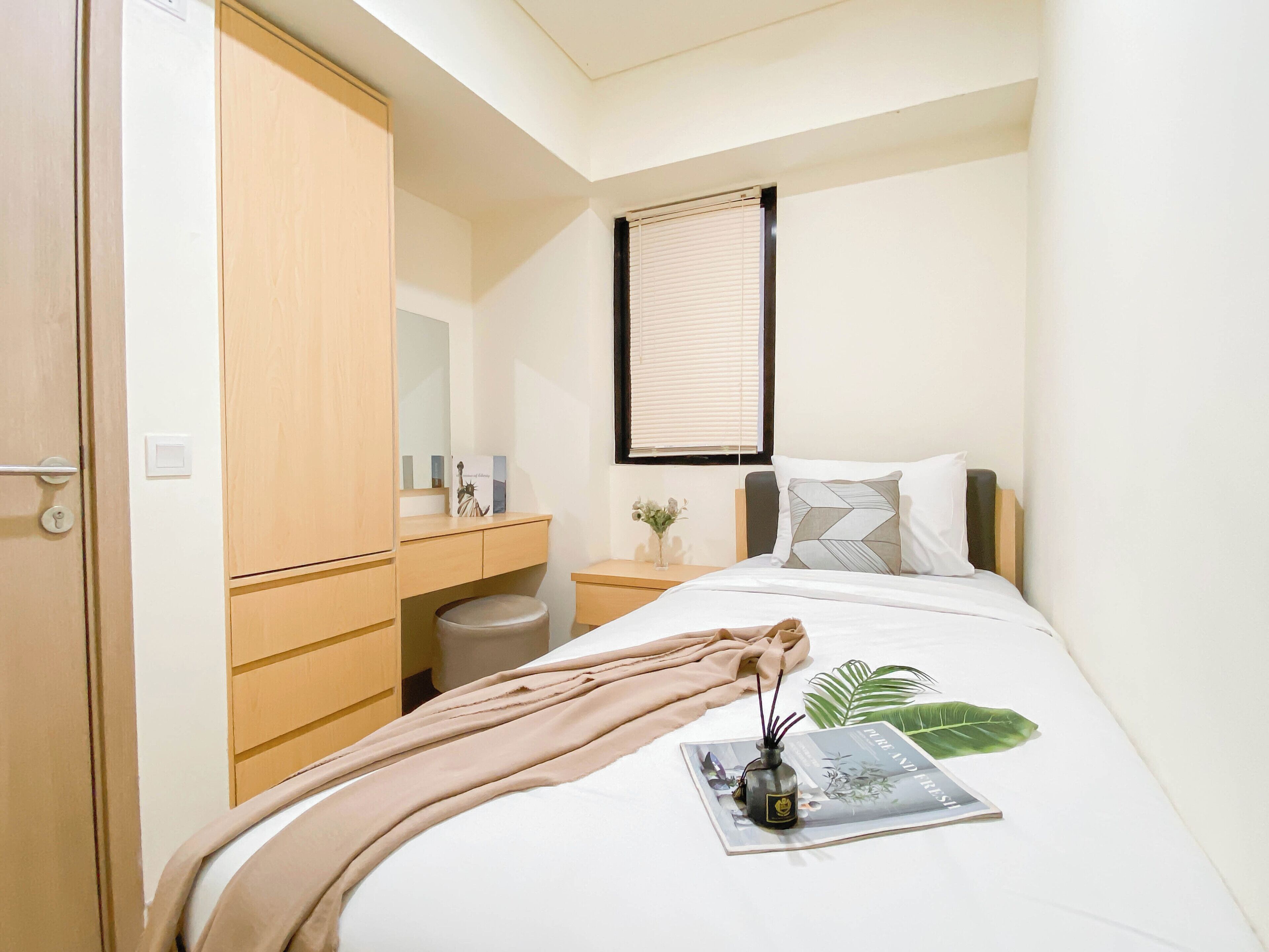 A hotel room with a bed, a bedside table, a nightstand, a wardrobe, and a window with blinds.