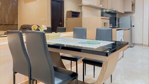 A modern kitchen with a built-in stove, a sink, and a refrigerator. There is a dining area with a glass-top table and black chairs. - Spacious And Comfy 1Br At L'Avenue Pancoran Apartment (Jakarta)