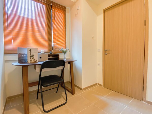 A small room with a desk, a chair, a window with blinds, a door, and a tiled floor.