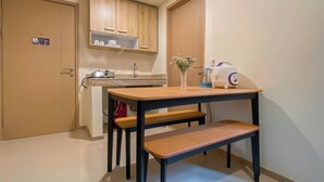 A compact kitchen with wooden cabinets, a sink, a kettle, and a small table with a bench.