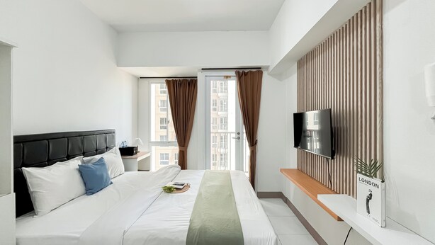 Een moderne hotelkamer met een groot bed, een flatscreen televisie aan de muur, een klein nachtkastje en uitzicht op de stad door het raam.