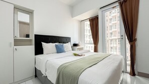 A hotel room with a bed, a nightstand, a window with curtains, and a view of buildings outside. - Comfort Studio At Tokyo Riverside Pik 2 Apartment (Teluknaga)