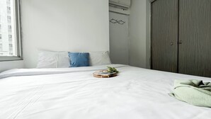 A neatly made bed with white bedding, a blue pillow, and a small plant on a tray. - Warm And Homey 2Br Apartment At Green Bay Pluit (Jakarta)