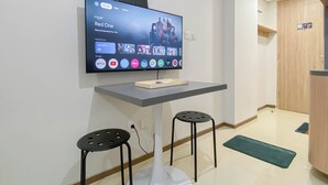 A flat-screen TV mounted on a wall above a small table with two stools. - Affordable And Homey Studio Room At Meikarta Apartment (Cikarang)