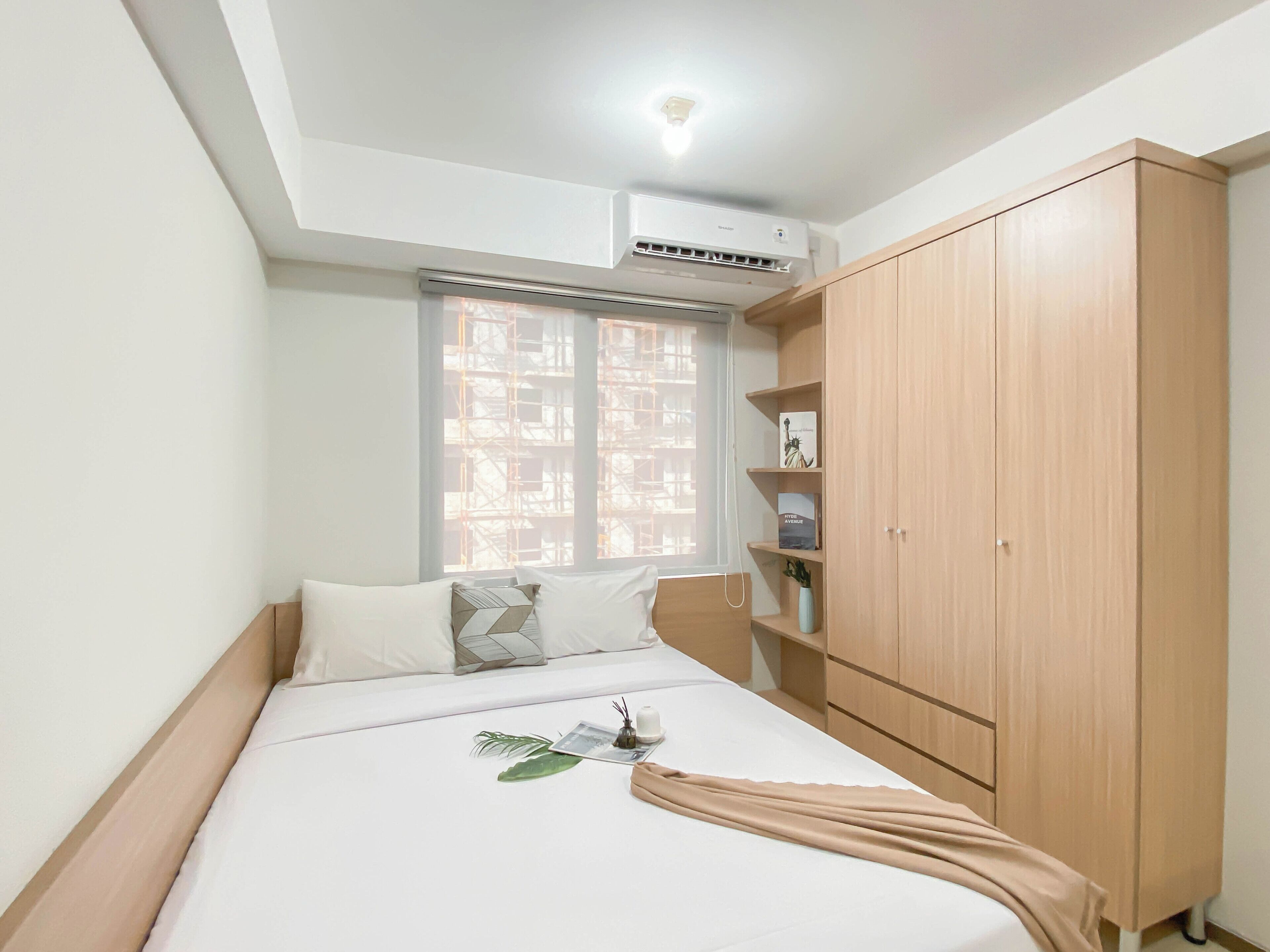 Een slaapkamer met een bed, een kledingkast, een raam met uitzicht op een bouwplaats en een airconditioning op het plafond.