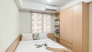 A bedroom with a bed, a wardrobe, a window with a view of a building under construction, and an air conditioning unit on the ceiling. - Affordable And Homey Studio Room At Meikarta Apartment (Cikarang)