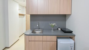 A compact kitchen with wooden cabinets, a stainless steel sink, a small refrigerator, and a vase with flowers on the countertop. - Affordable And Homey Studio Room At Meikarta Apartment (Cikarang)