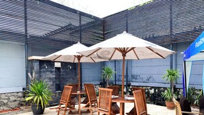 Eine Terrasses mit Holztischen und -stühlen, zwei Sonnenschirmen und Blumentöpfen.