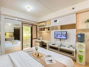 A hotel room with a bed, a desk with a computer, a TV, and a water dispenser. - Affordable Studio At Metropark Condominium Jababeka Apartment (Cikarang)