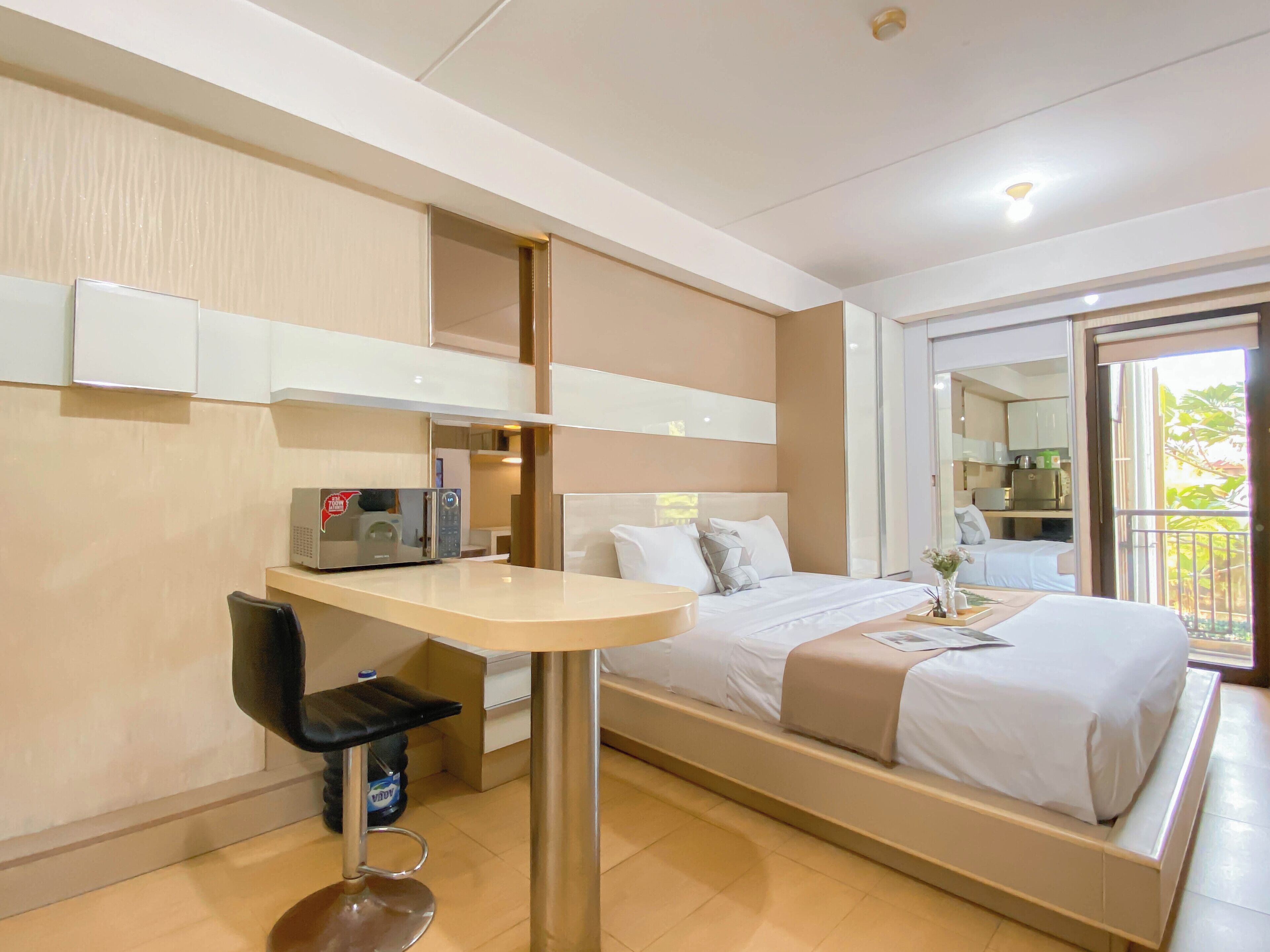 A hotel room with a bed, a desk, a chair, a microwave, and a balcony with a view.