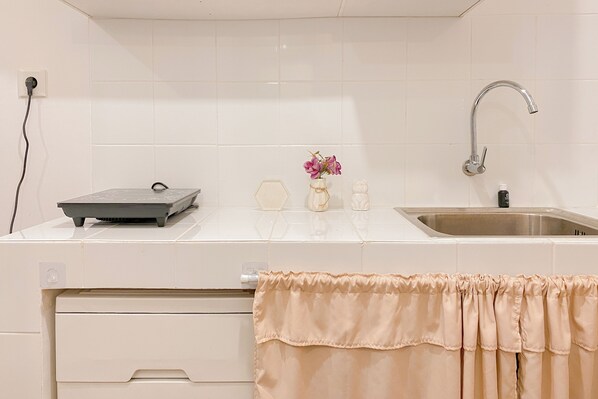 Une cuisine avec des carreaux blancs, un évier en acier inoxydable, un robinet, un petit vase avec des fleurs et une multiprise.
