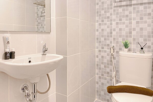 A bathroom with a white sink, a mirror, a toilet, and a small potted plant on the toilet tank. - Best Studio Room At Tokyo Riverside Pik 2 Apartment (Teluknaga)
