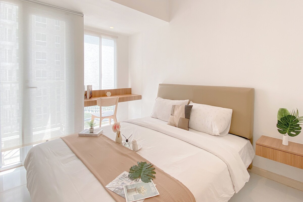 Une chambre à coucher moderne avec un grand lit, une table de chevet, une fenêtre avec des rideaux et une plante en pot.
