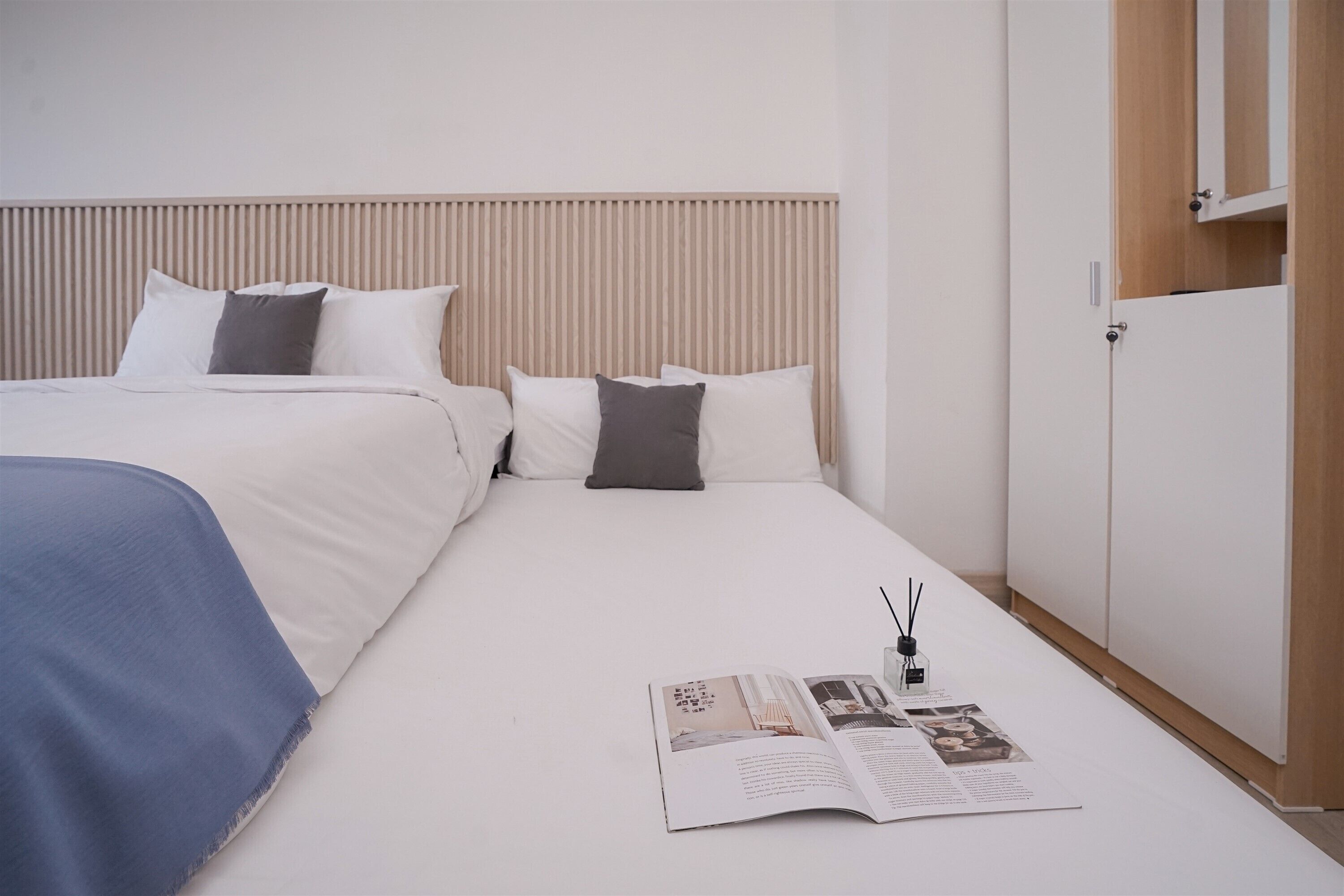 Een netjes opgemaakt bed met een tijdschrift erop, een houten hoofdbord en een kledingkast op de achtergrond.