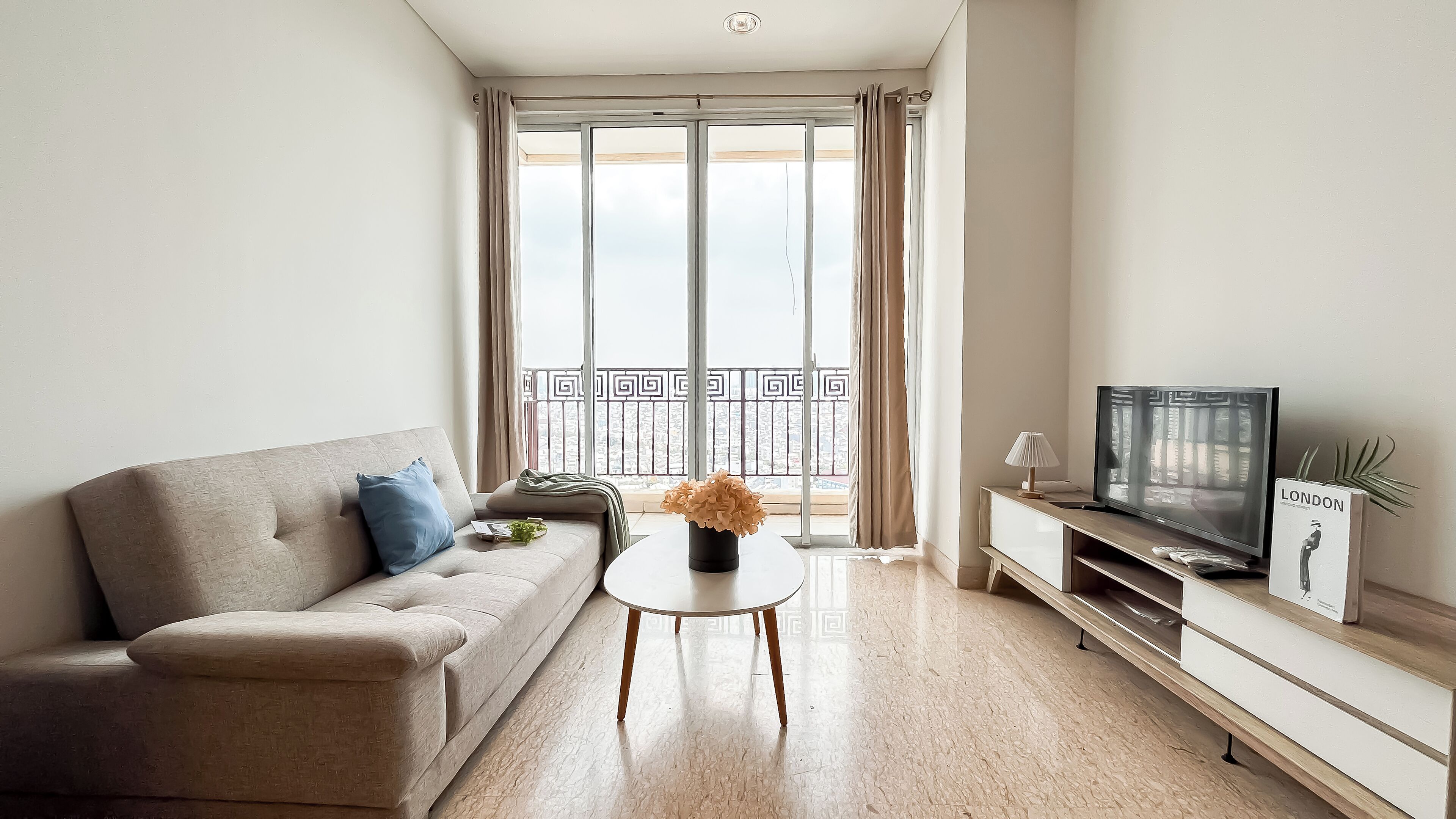 A modern living room with a sofa, a coffee table, a TV, and a balcony with a view.